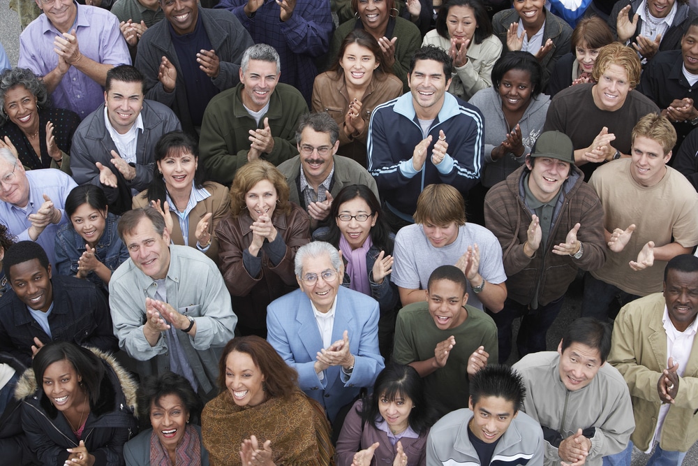Bird perspective image of a large group of paid clinical trial participants looking up and clapping with their hands.