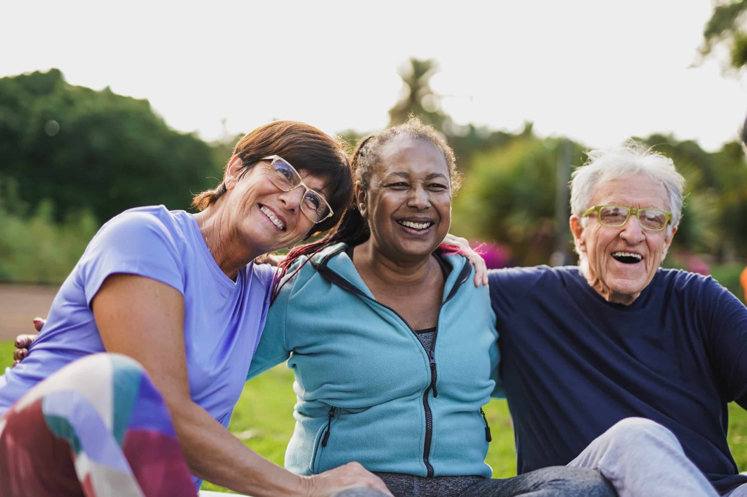 Happy elderly paid clinical trial participants hugging each other outdoor.