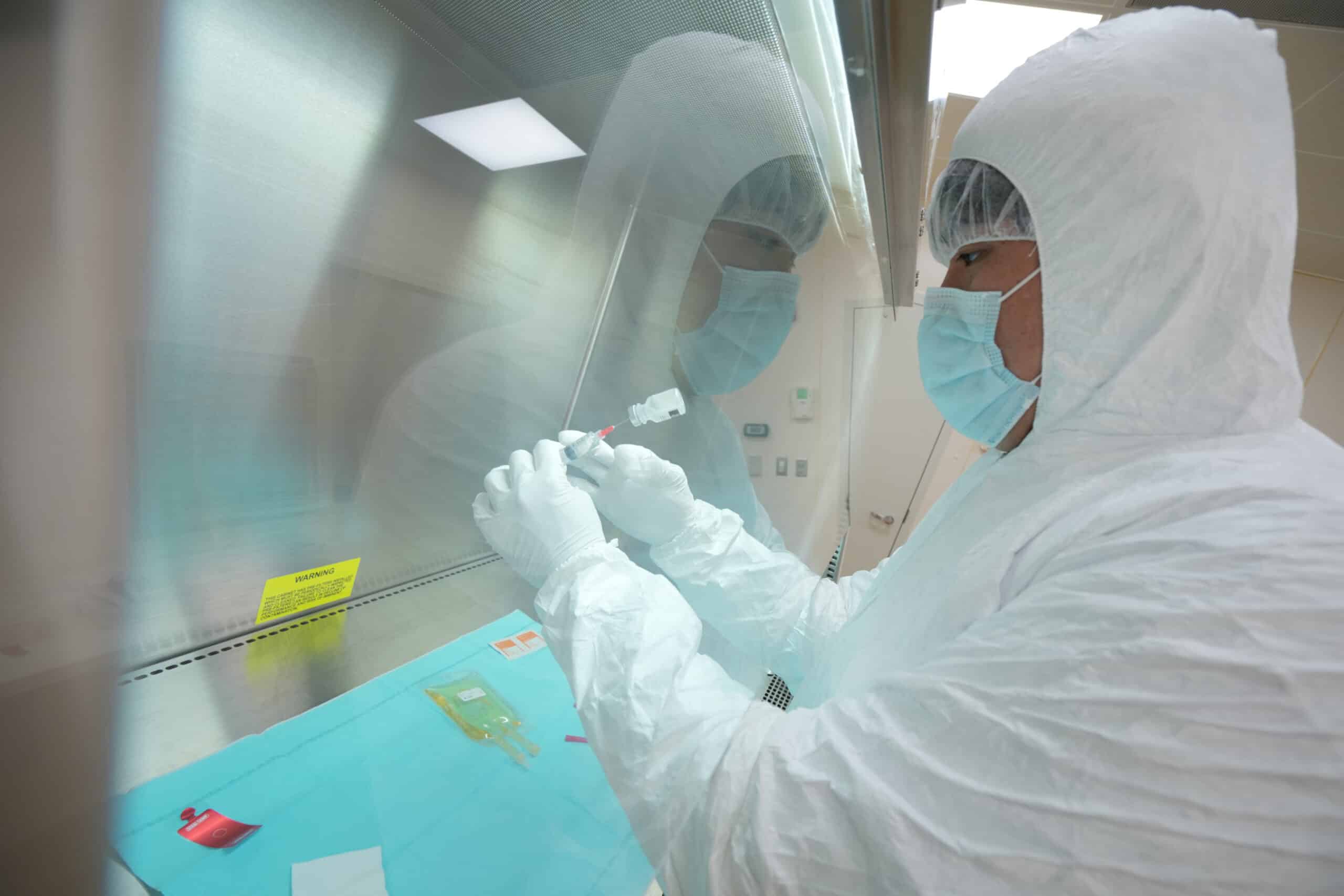 Clinical trial researcher in a coverall taking a dose of a medicine with a syringe.