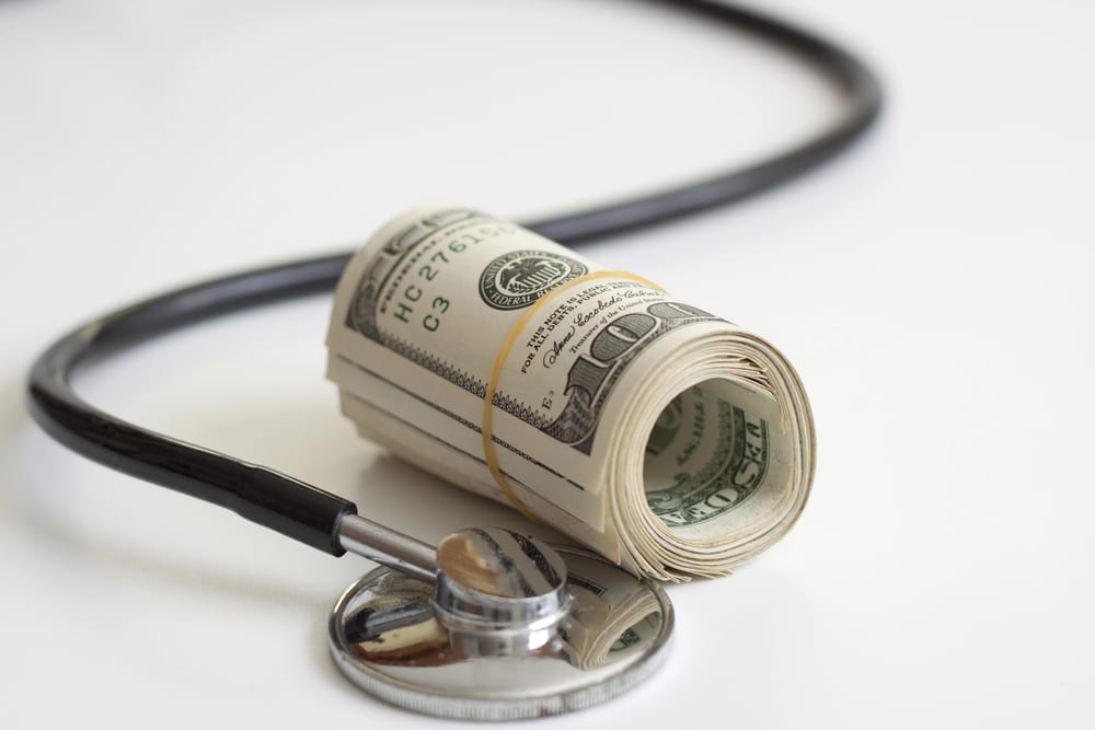 A stethoscope and a roll of American dollars held by rubber band.